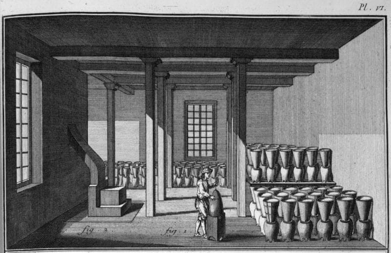 Uma refinaria de açúcar, imagem de 1762 Uma refinaria de açúcar, imagem de 1762. Nesta ilustração, o melaço está a ser drenado do açúcar. Os pães de açúcar estão nos tachos em forma de cone, virados ao contrário, cada um com um orifício no fundo (ver imagens abaixo). O melaço escorria dos tachos em forma de cone para os tachos redondos por baixo deles. Imagem de uma enciclopédia de Denis Diderot, 1751 a 1775 (Slavery Images, domínio público).